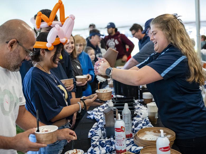 Alumnus wearing balloon animal hat gets Berkey Creamery ice cream from another alumnus